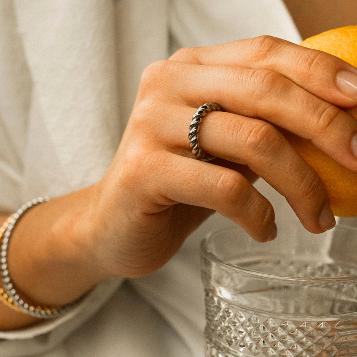 Elegant hand wearing AN JEWELS JEWELRY Mod. AAC.R05S-8 silver ring holding a bright orange near a glass.
