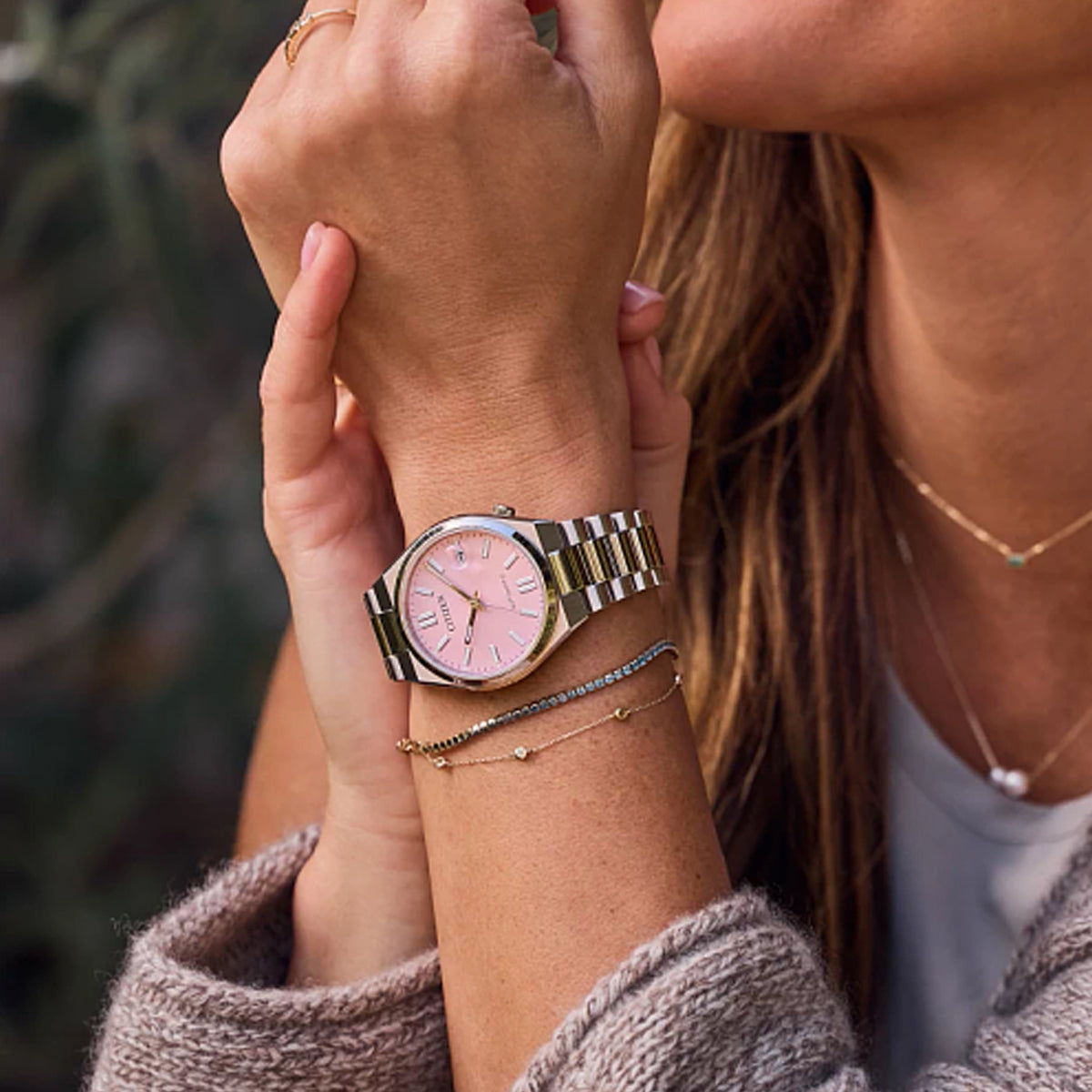 CITIZEN MOD. NJ0200-50Z wristwatch on woman's wrist with pink dial and stainless steel bracelet, outdoor setting