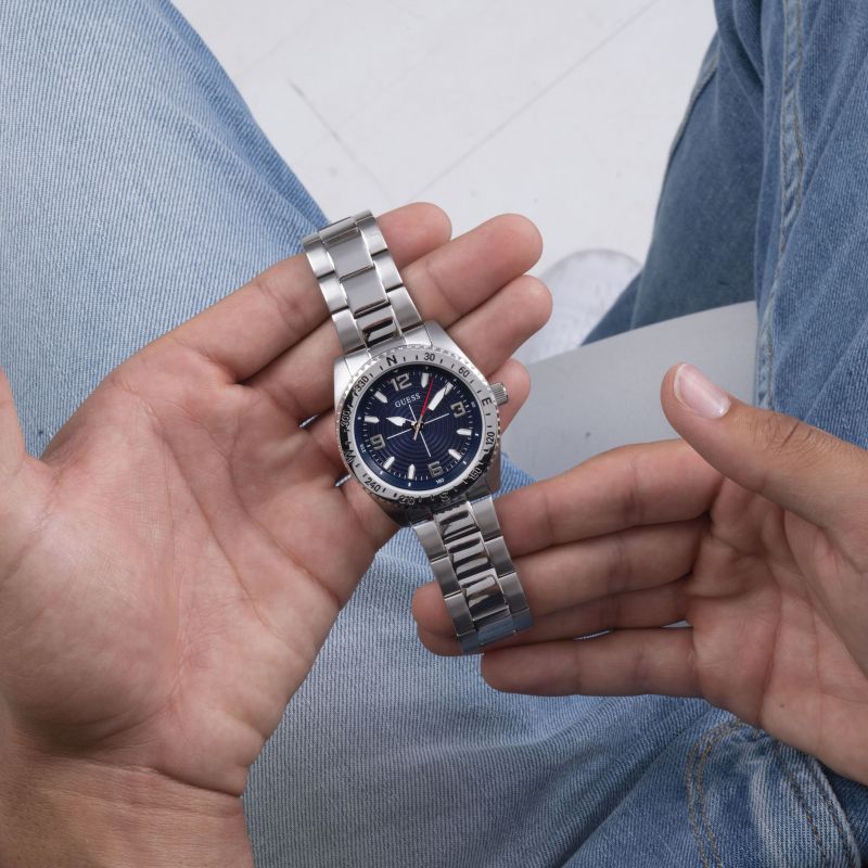 Hand holding GUESS Mod. GW0327G1 quartz analog watch with silver 925° material and mineral dial, showing water resistance of 5 ATM.