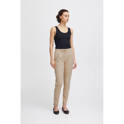 Woman modeling ICHI Beige Polyester Pants with elastic waistband and drawstring, showcasing slim fit and front pleats for modern style and comfort.