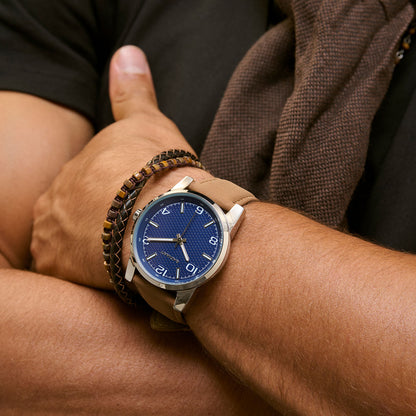 Close-up of a man's wrist wearing a stylish blue-faced round watch and a brown beaded bracelet, showcasing fashion accessories.